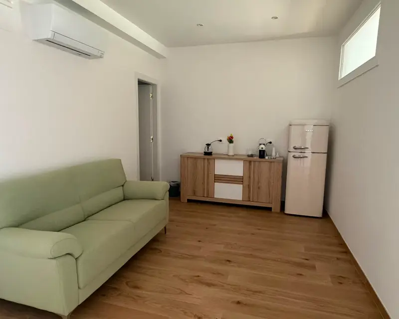 La zona relax con divano verde salvia, credenza e frigorifero
